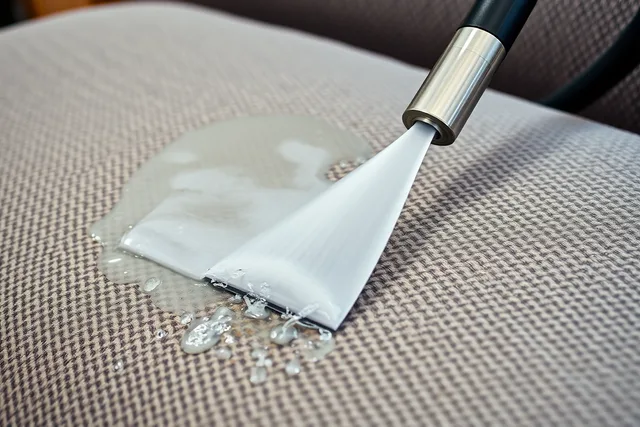Upholstery cleaning wand extracting dirt from a gray fabric couch cushion. Leather vs Fabric Couch Cleaning: Which Costs Less Over Time?